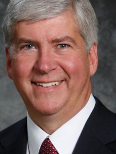 A headshot of Governor Snyder. He has a big smile on his face, salt and pepper closely cropped hair and a suit with a red tie.