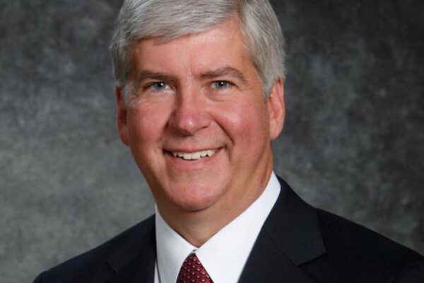A headshot of Governor Snyder. He has a big smile on his face, salt and pepper closely cropped hair and a suit with a red tie.