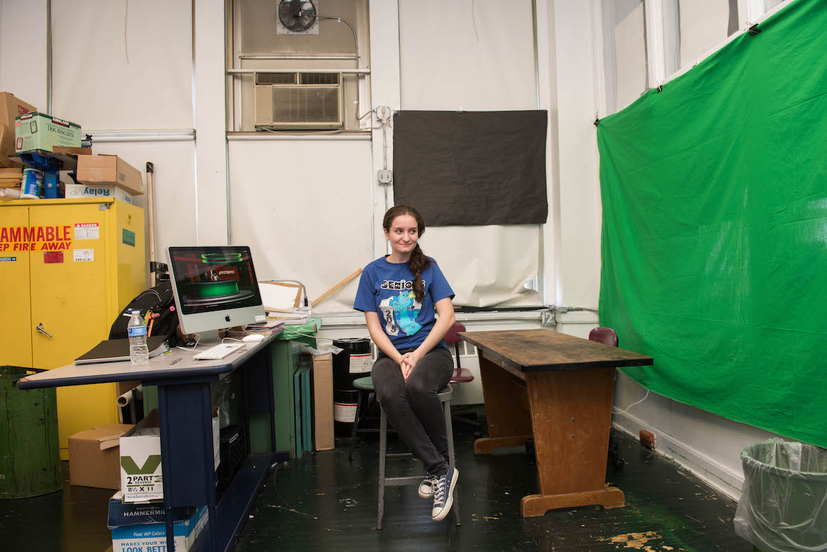 Elsa Nilay, a senior at Hamtramck High School, helps direct the school's daily news programming. A makeshift green screen stretches across a wall to her left.
