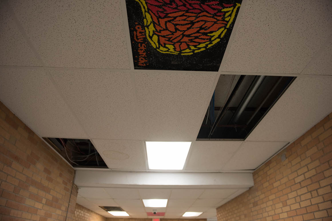 As an art activity, students paint the particle board on the ceiling to conceal the brown water stains left by the school's leaking roof.