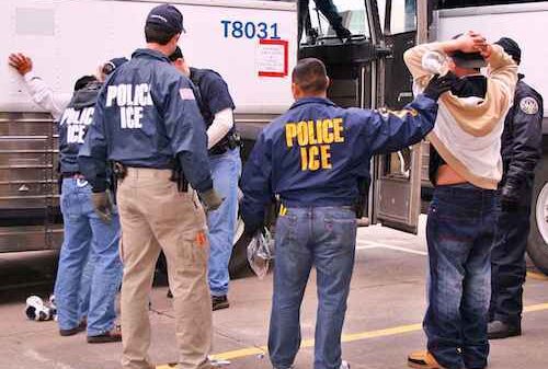 police and ICE officer arresting person with their hands up
