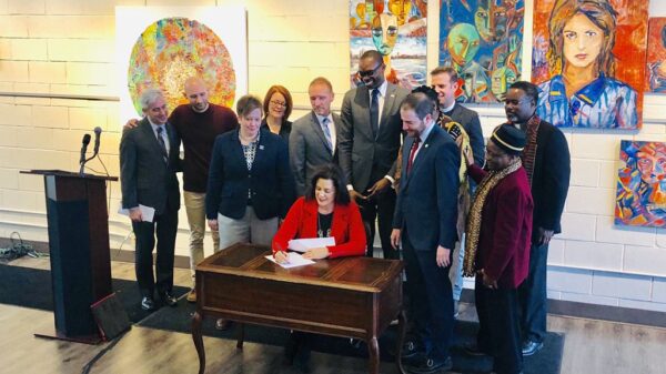 Governor Gretchen Whitmer signs executive directive at desk with supporters to ban state government from discriminating against LGBT community