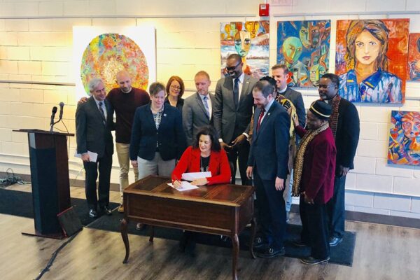 Governor Gretchen Whitmer signs executive directive at desk with supporters to ban state government from discriminating against LGBT community