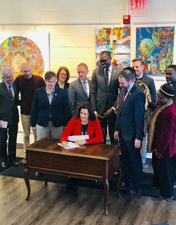 Governor Gretchen Whitmer signs executive directive at desk with supporters to ban state government from discriminating against LGBT community