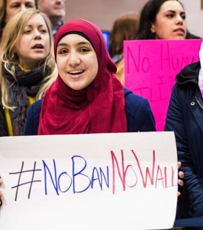woman wearing hijab holds sign that says "No Ban, No Wall"