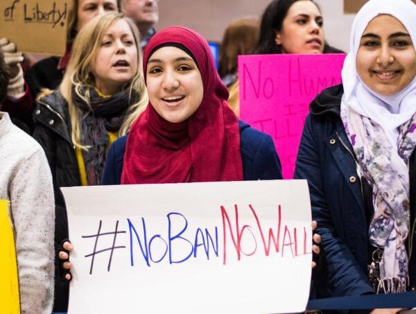 woman wearing hijab holds sign that says "No Ban, No Wall"