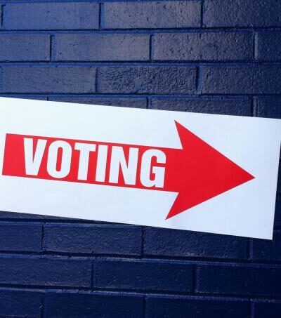 Sign that reads voting against blue brick wall