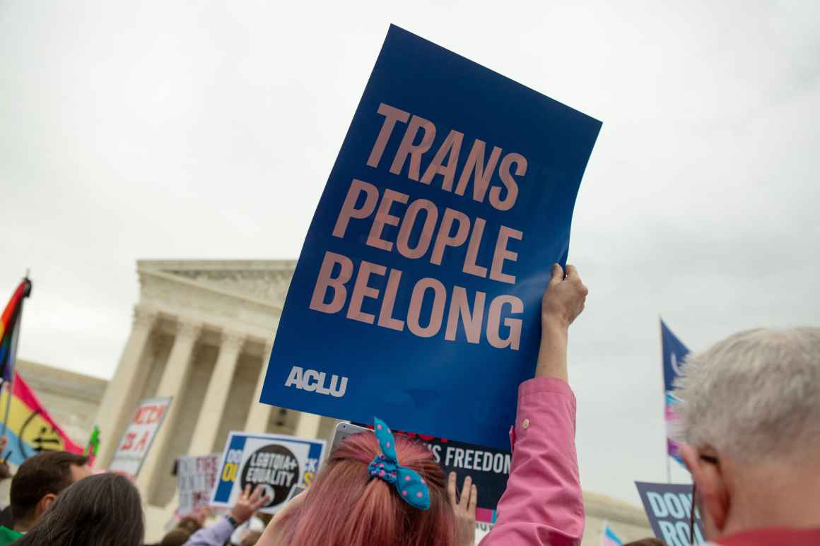 An activist holds up a sign that reads 'Trans People Belong'