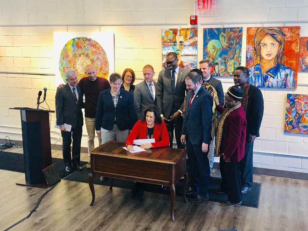 Governor Gretchen Whitmer signs executive directive at desk with supporters to ban state government from discriminating against LGBT community