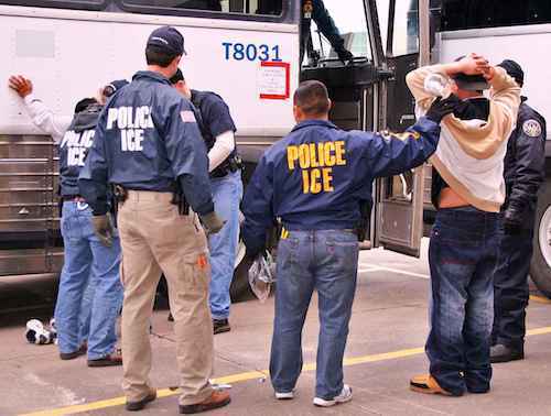 police and ICE officer arresting person with their hands up