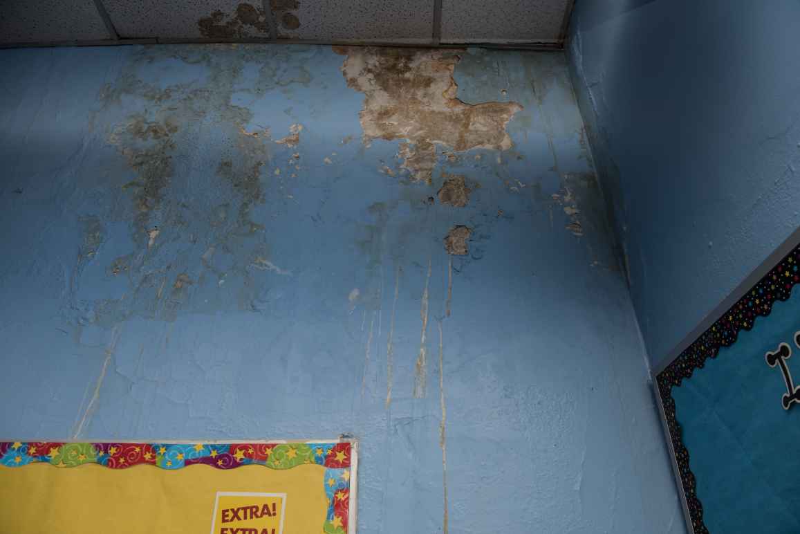 The corner of a blue wall and dropped ceiling with water damage. On the left is a bulletin board with yellow paper covering it and a starry border and on the right is a bulletin board with blue paper