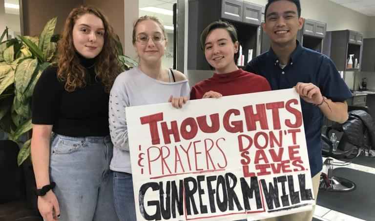 Students holding sign reading "Thoughts and prayers don't save lives, gun reform will"