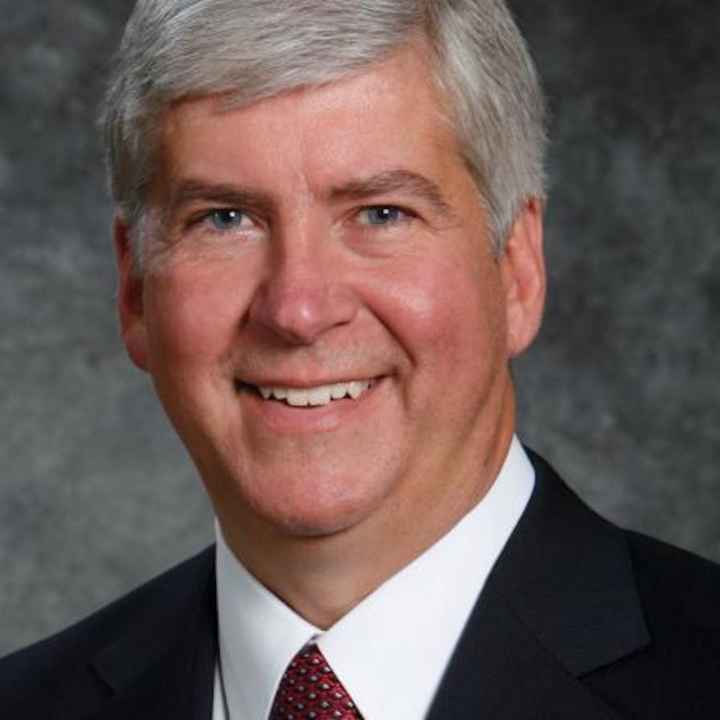 A headshot of Governor Snyder. He has a big smile on his face, salt and pepper closely cropped hair and a suit with a red tie.