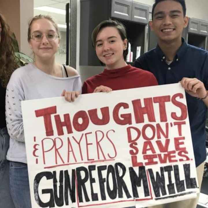 Students holding sign reading "Thoughts and prayers don't save lives, gun reform will"